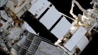 two astronauts in space suits work on the outside of a space station