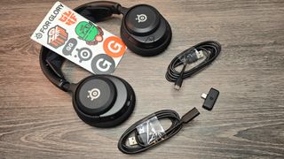 A photo showing the accessories included with the SteelSeries Arctis Nova 4 Wireless headset on a wooden surface.