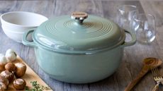 Lodge Dutch Oven in Sage on a wooden table next to a chopping board of mushrooms