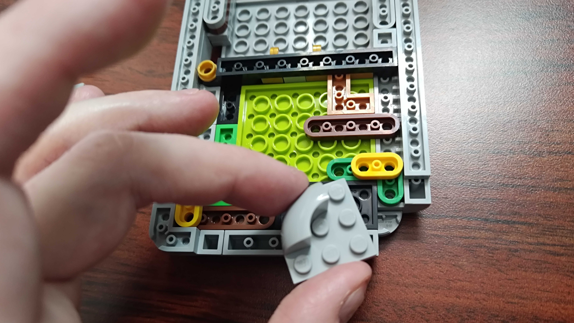 A hand holds a piece for the Lego Game Boy mid-build