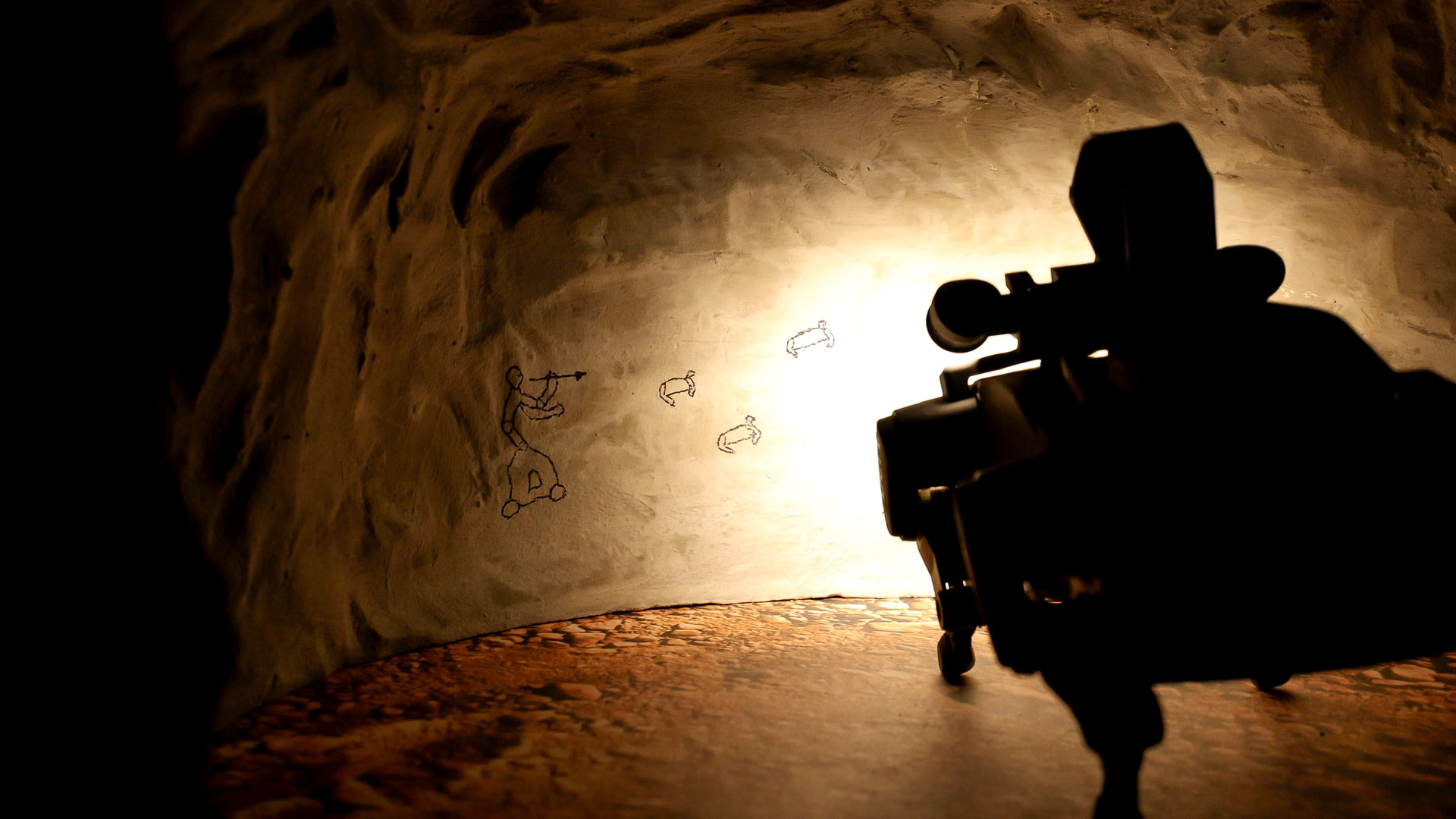 A four-legged robot shines a light on the wall of a cave with drawings on it