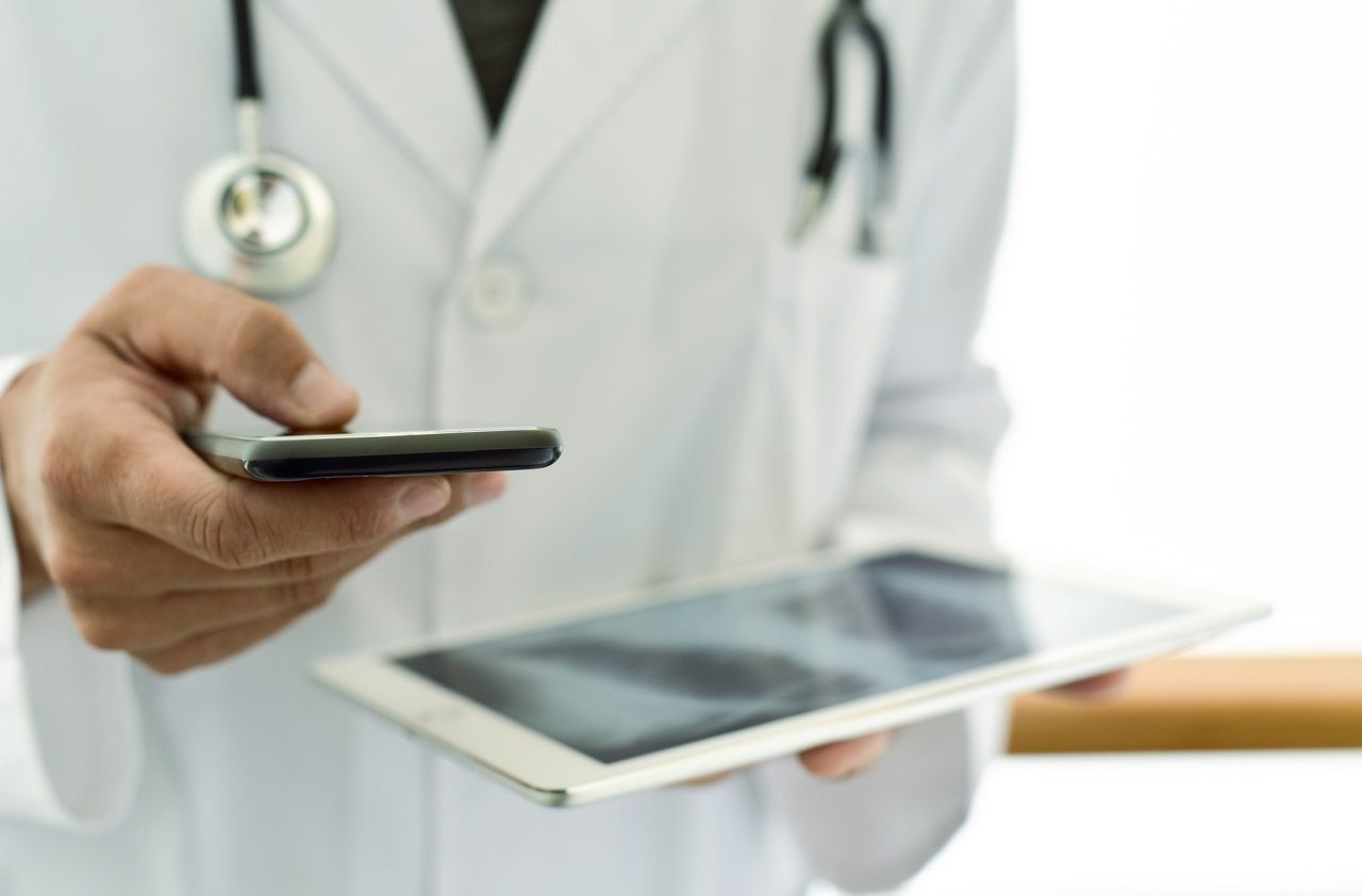 closeup of a young caucasian doctor man wearing a white coat using a smartphone while is checking a chest radiograph in a tablet computer