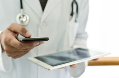 closeup of a young caucasian doctor man wearing a white coat using a smartphone while is checking a chest radiograph in a tablet computer