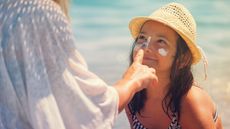 A mother applies sunscreen to her smiling daughter's nose.