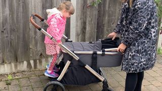 Image of a toddler standing on a pram board with mum holding pram