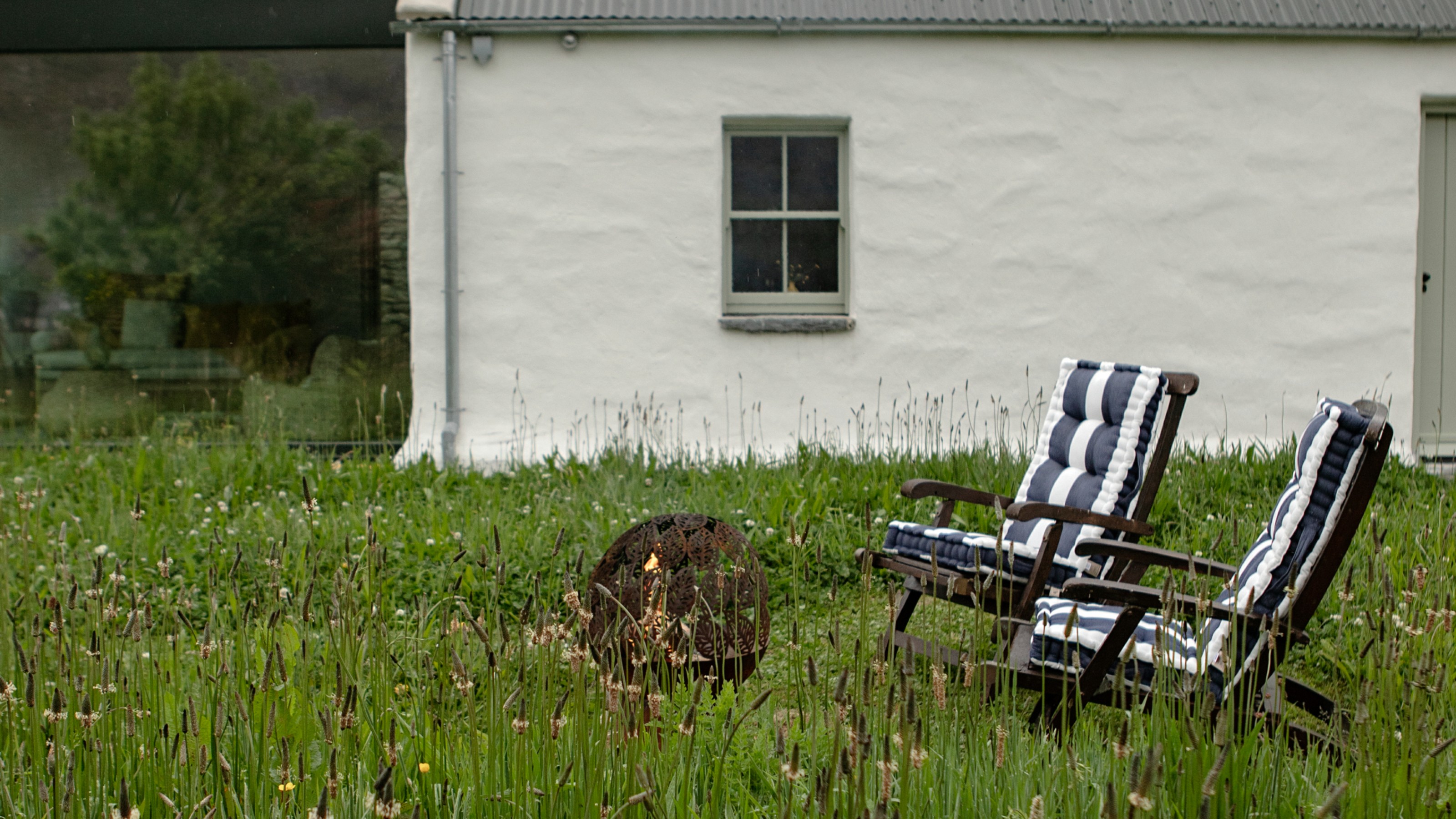 A garden with a firepit and two dark wood adirondack garden chairs with striped seat and back cushions