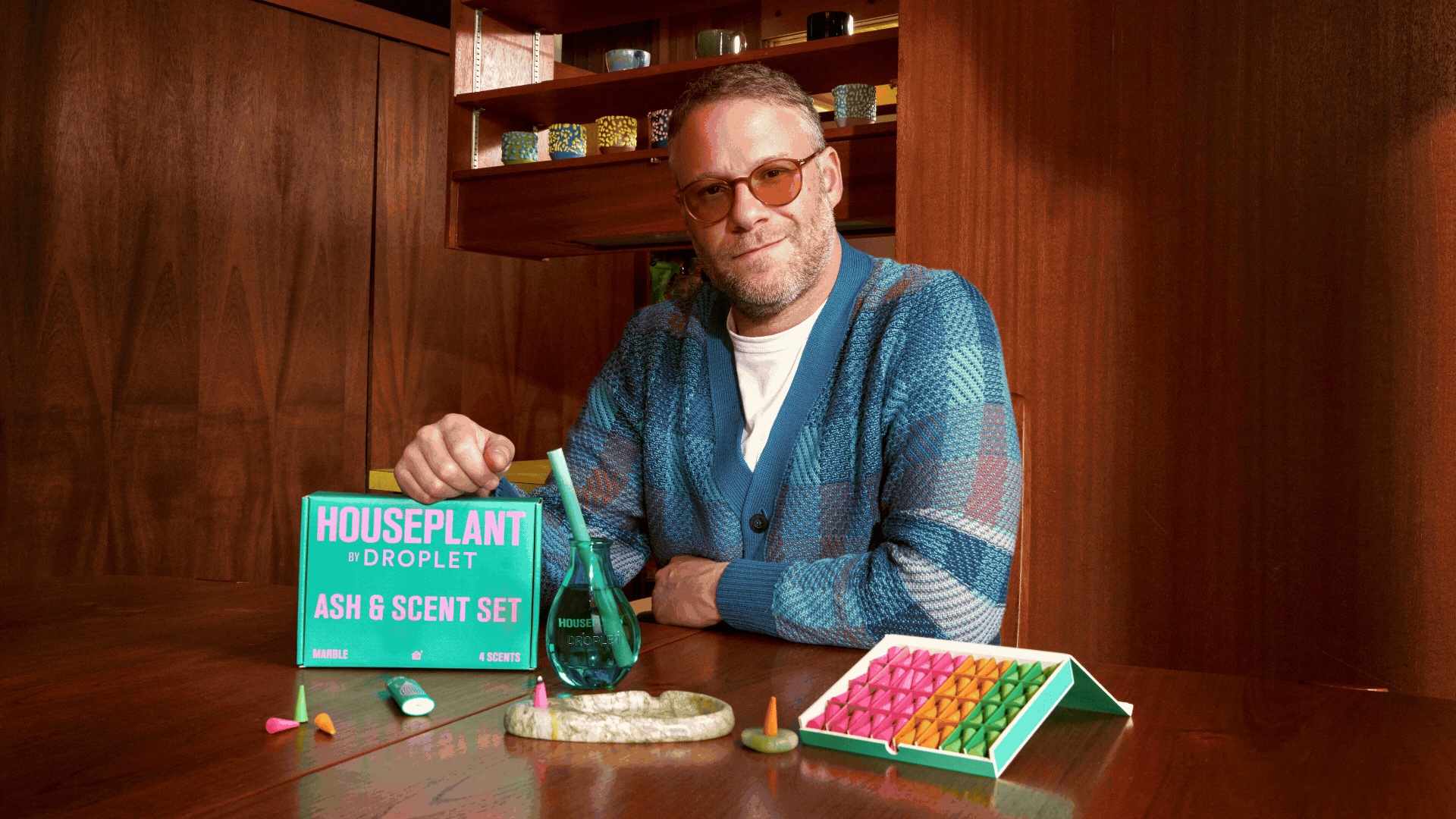 A GIF of Seth Rogen beside colorful incense cones and a green glass reed diffuser from Houseplant x Droplet