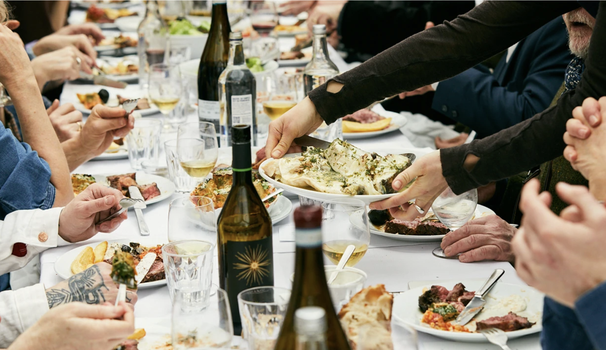 an image of a long table in a white tablecoth with people sitting either side and plenty of plates and wine on the table at Rochelle Canteen