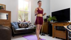 Woman standing in a living room in sportswear, holding the ends of a yellow resistance band