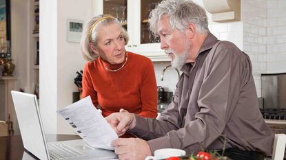 two older adults looking at a computer screen and paperwork