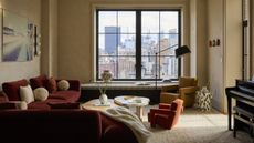A living room with cream walls, a red sofa, and an orange accent chair next to a coffee table