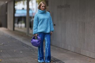 woman in blue oversized sweater, blue velvet pants, and silver shoes