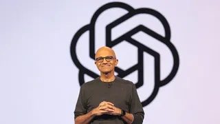 Satya Nadella standing on stage in front of the OpenAI logo during a Microsoft event.