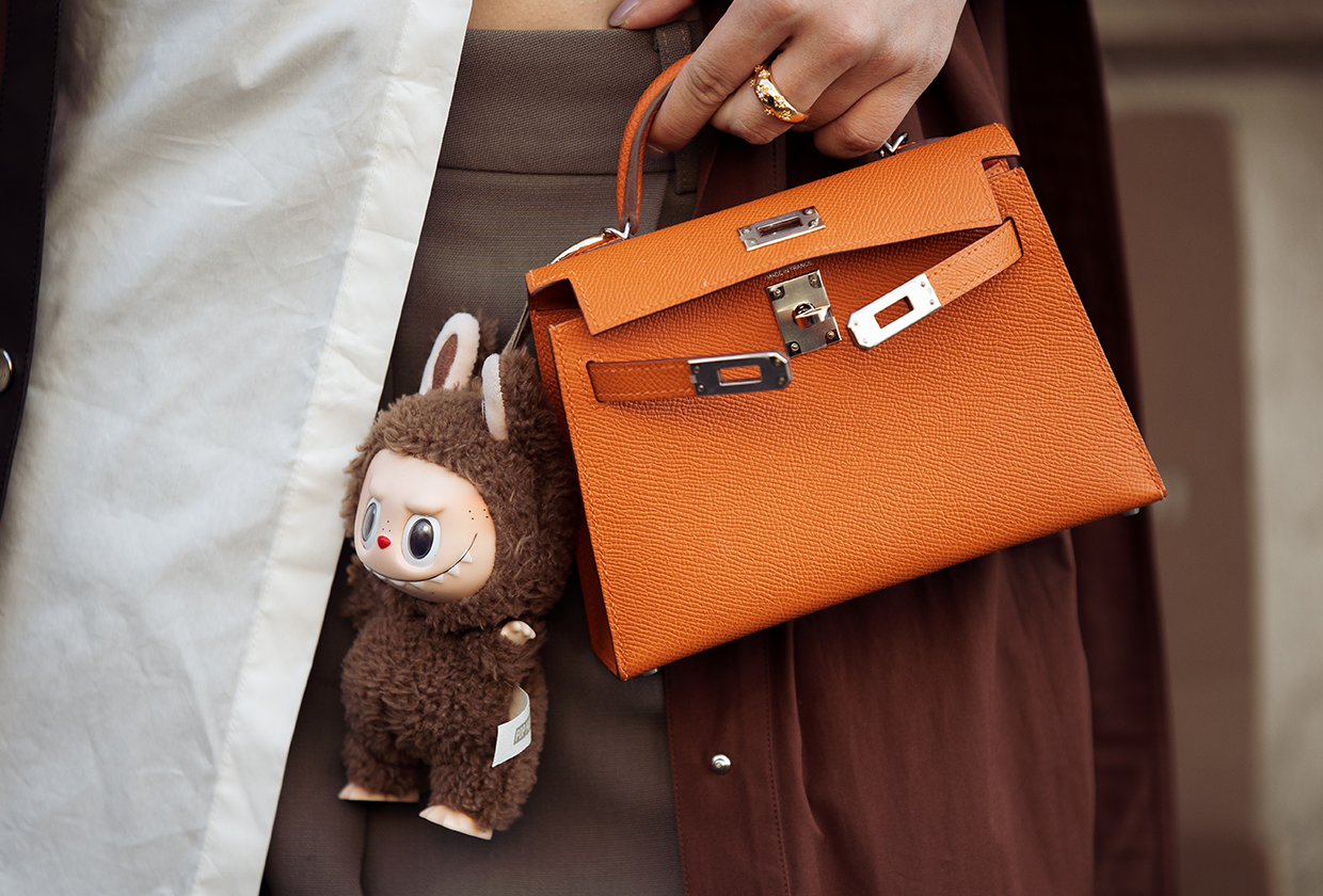 Woman wearing luxury handbag with Labubu bag charm.