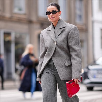 A woman walks at fashion month wearing a gray two piece suit with a red bag to illustrate a guide to the best tailored trousers