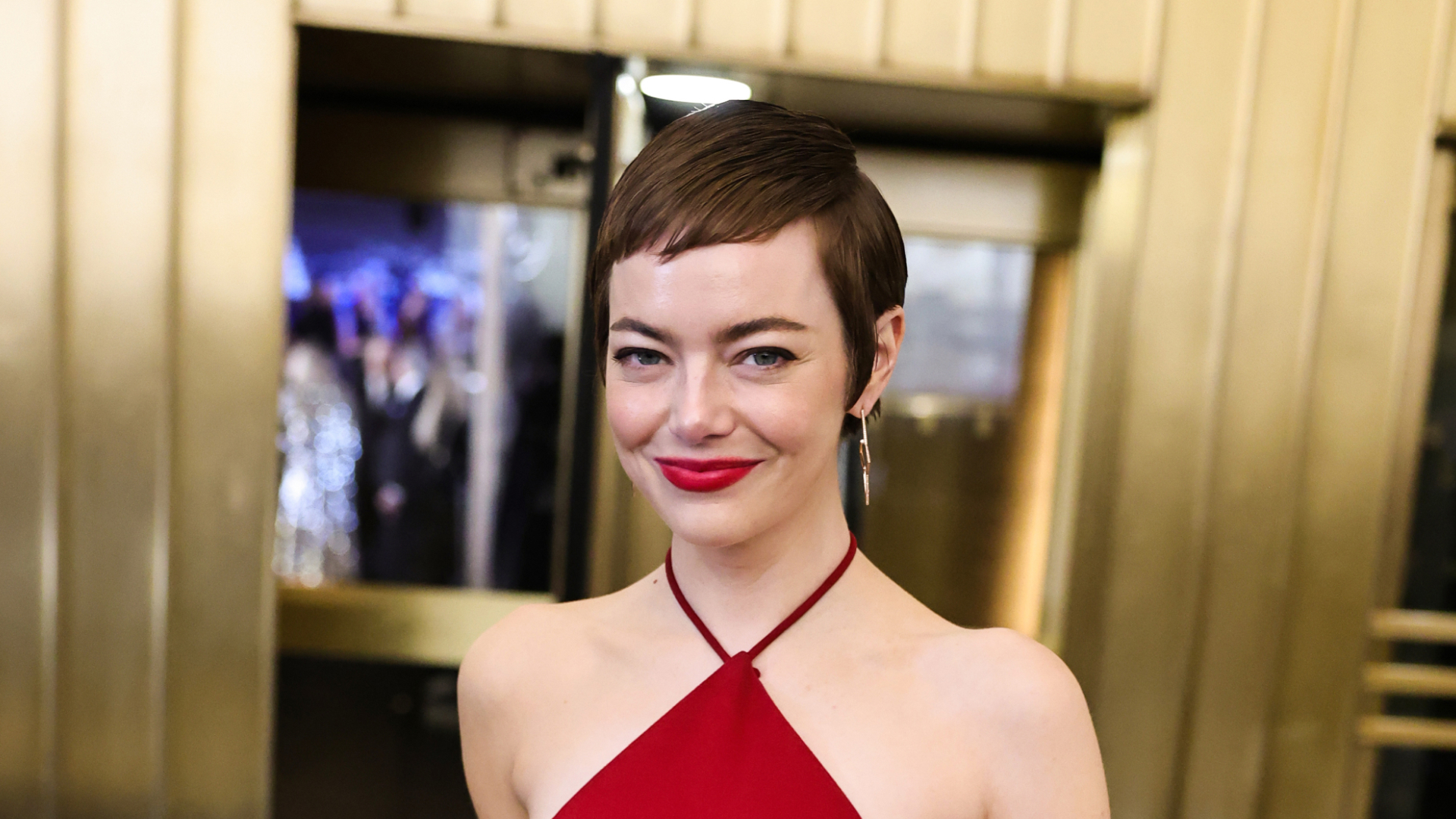 Emma Stone wearing red lipstick and a red dress, smiling at a camera