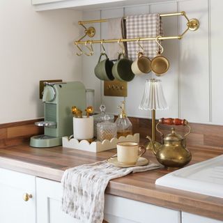 A kitchen counter with a sage green coffee machine, a scalloped tray, mugs and a wireless lamp