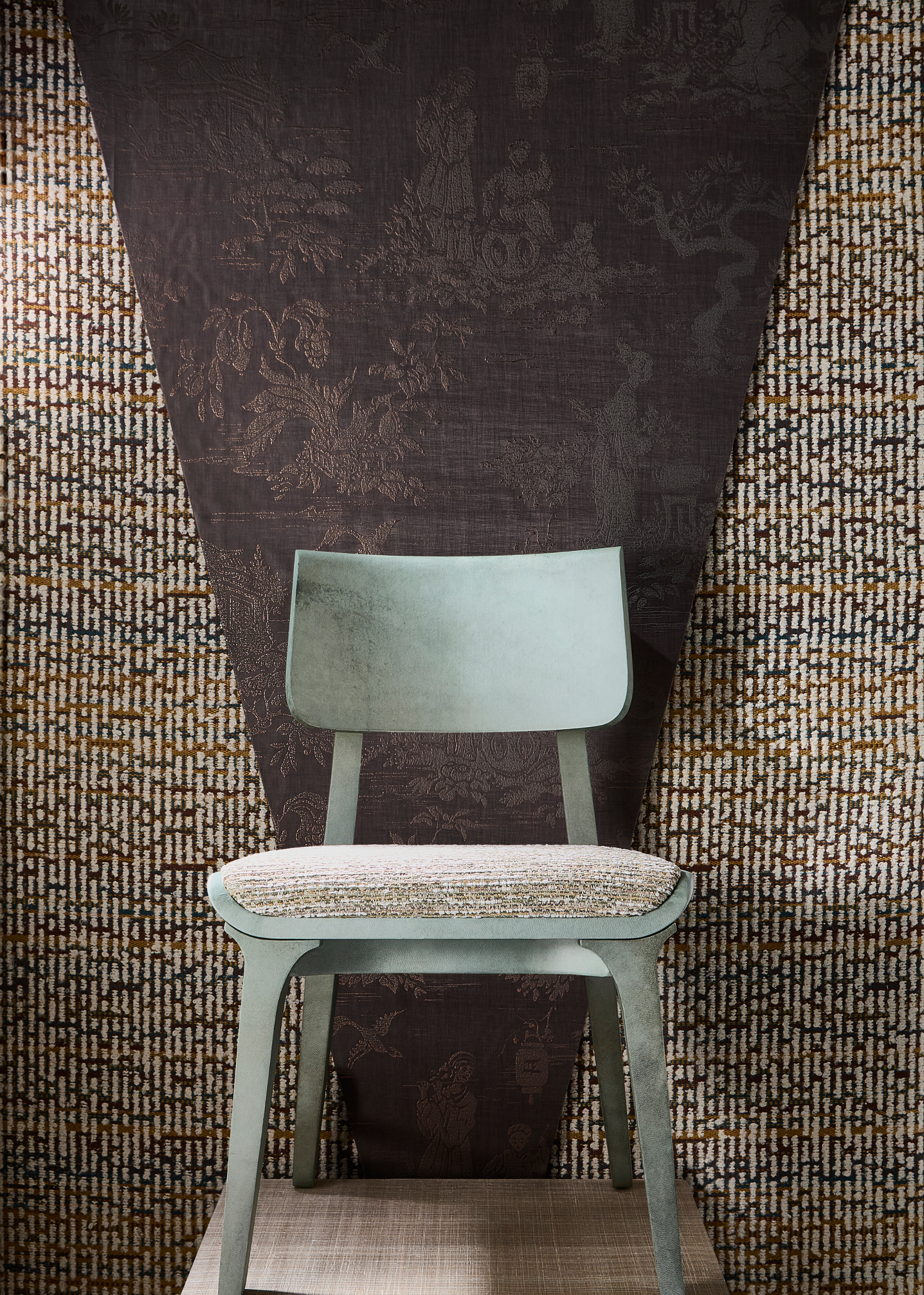 a design showcase featuring a mint green framed chair with a natural, almost woven seat against a backdrop that looks similar to the style and colouring of the chair&#039;s seat with a dark brown material or wallpaper over the top in a triangle shape behind the chair