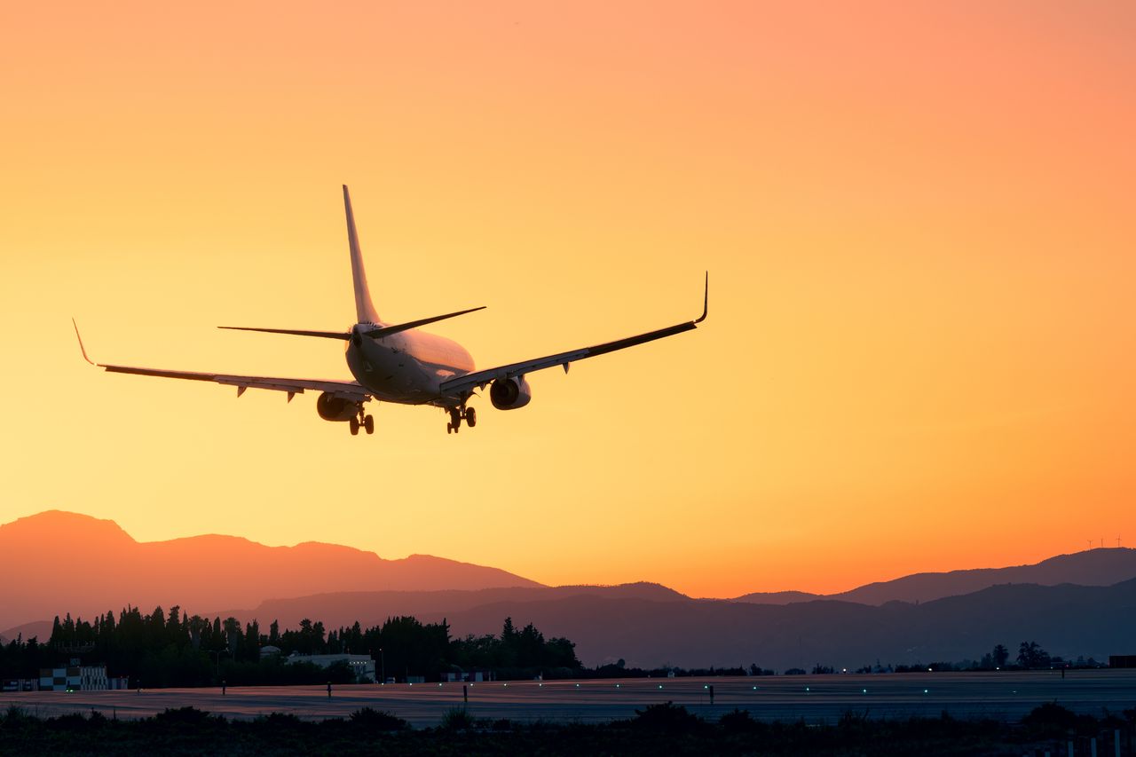 A plane flies into a sunset