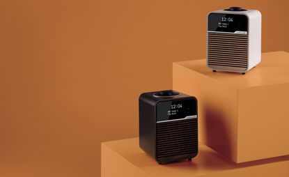 2 bluetooth radio speakers, the one one the left is black and one on the right is white. Both placed on orange boxes with an orange background