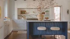 cream kitchen with blue fluted island and cream bar stools with large terracotta vase filled with stems