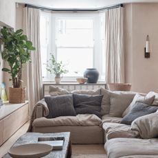A neutral living room with a corner sofa and full-length curtains framing the bay window