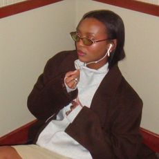 Devin Apollon wearing a brown jacket, gray zip-up, khaki skirt, and brown buckle boots