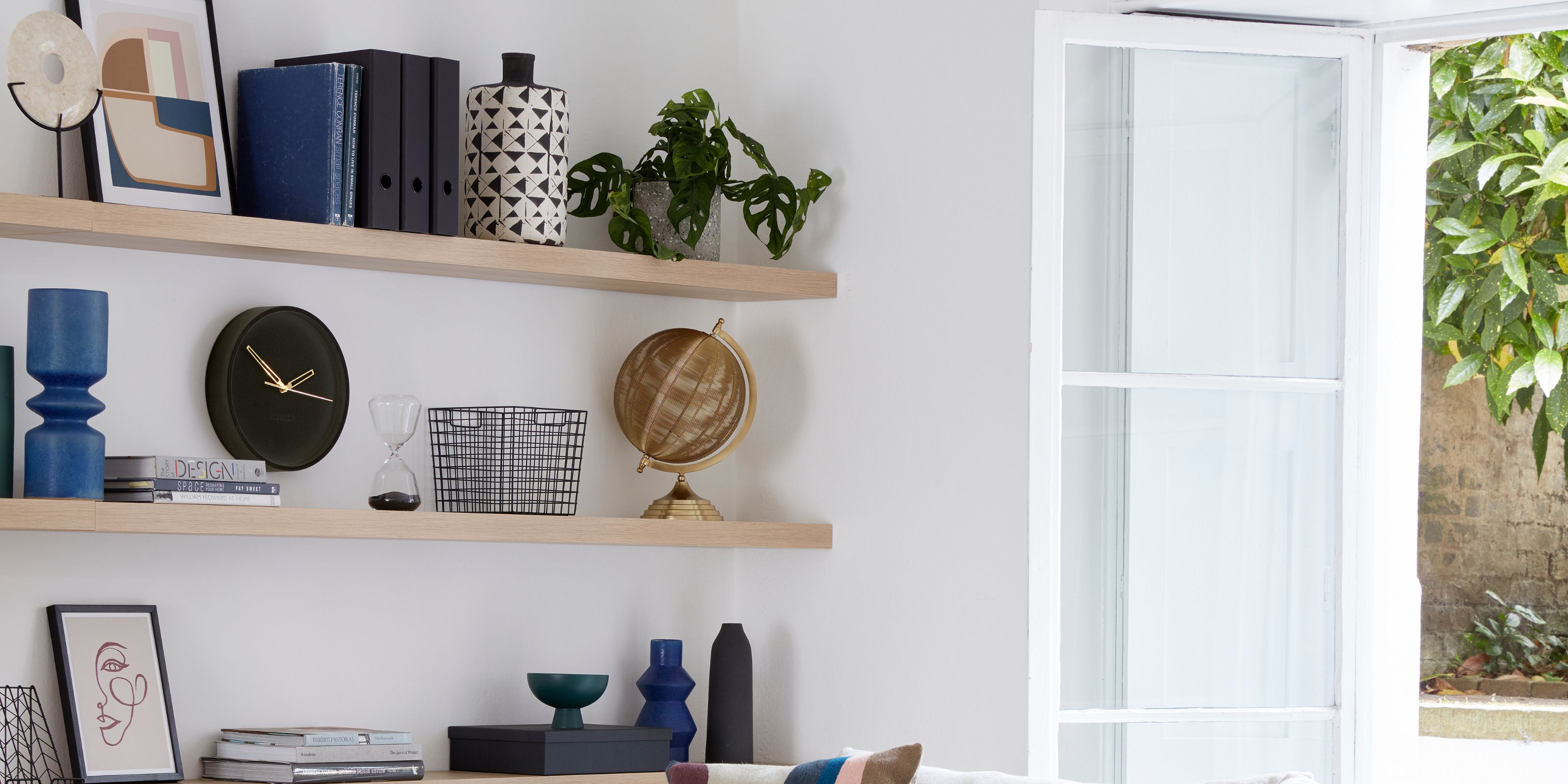 Three wooden shelves on a white wall next to an open window