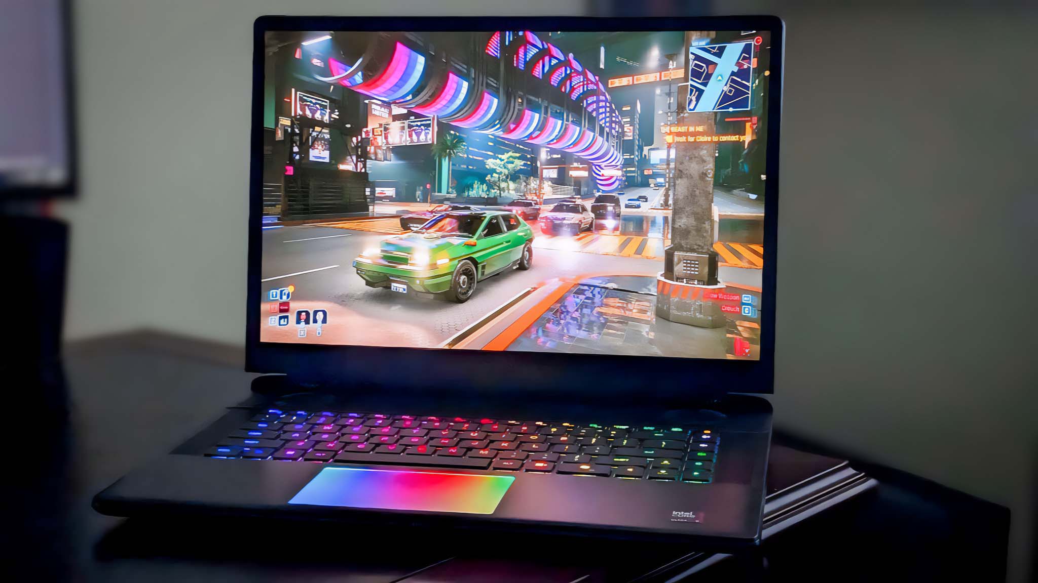 Alienware Area-51 16 gaming laptop running Cyberpunk 2077 with RGB touchpad and keyboard lit up.