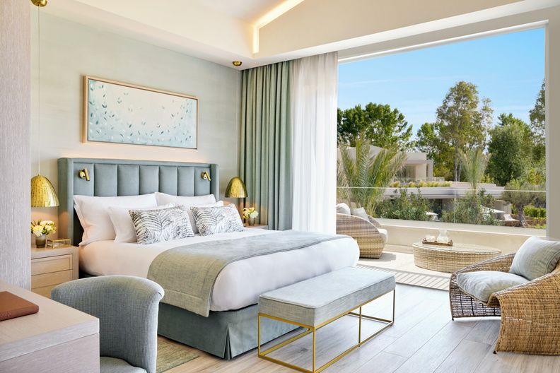 A standard double room at Porto Sani in Sani Resort. The bedroom is decorated in pale stones and blues and leads to a balcony with a table and chairs