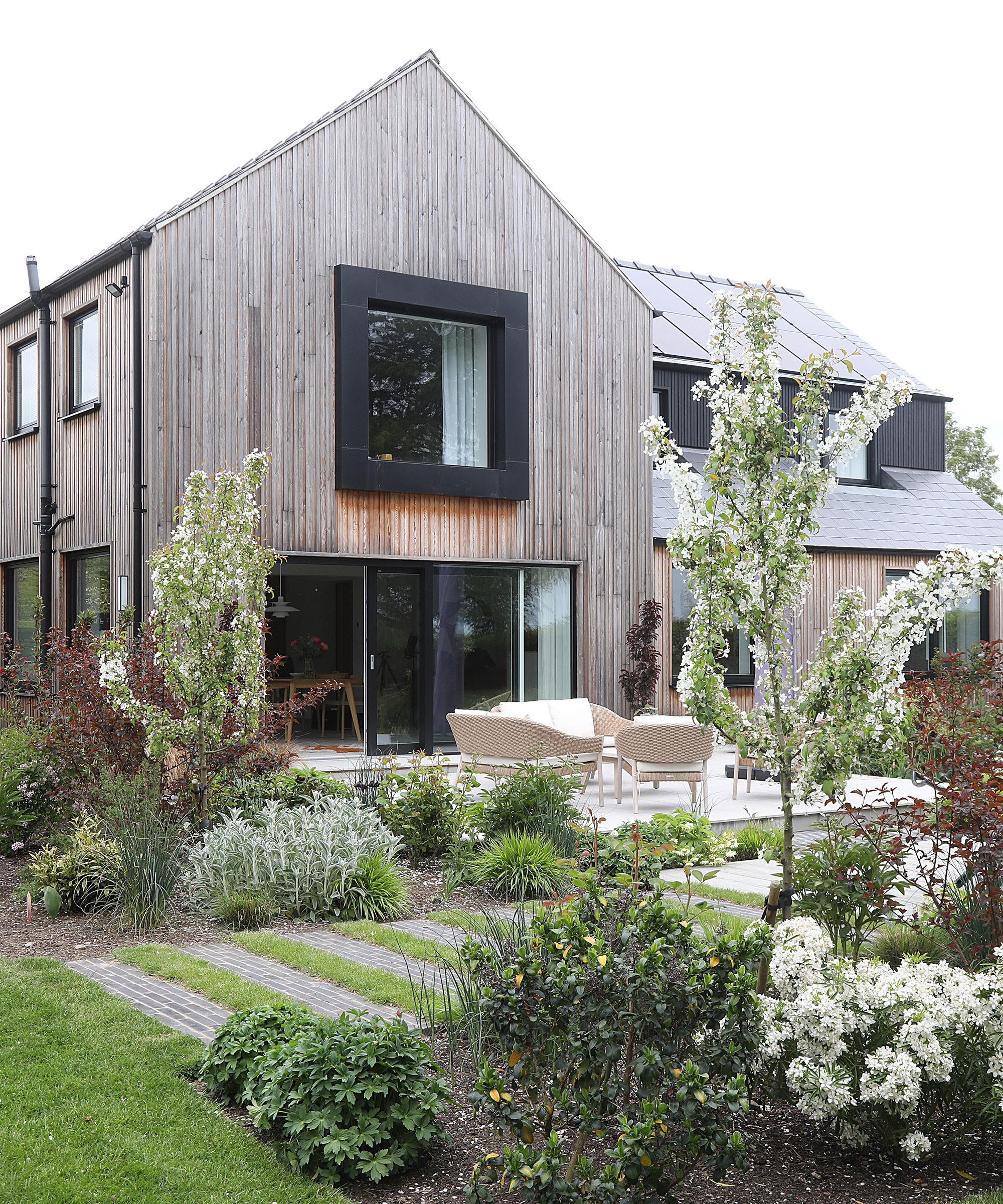 Exterior view of a newly renovated 1980s home with timber and dark cladding and landscaped garden