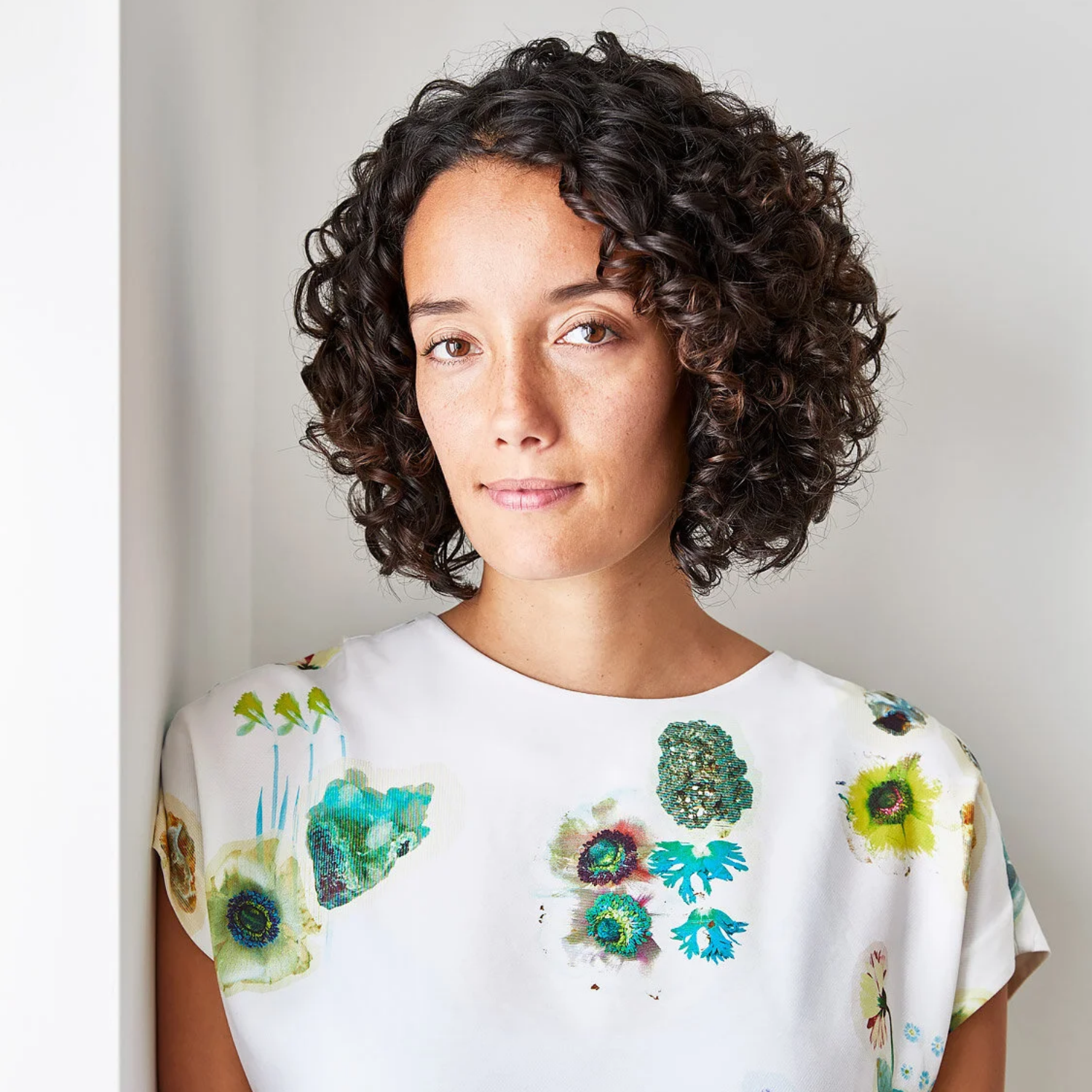A woman with short curly hair is in a white floral top