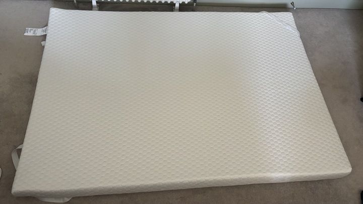 The Helix Premium Memory Foam Mattress Topper with GlacioTex left to expand on a carpeted floor.