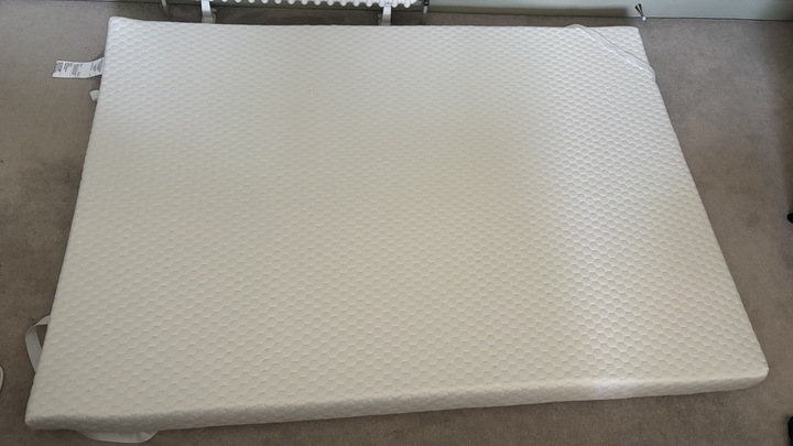 The Helix Premium Memory Foam Mattress Topper with GlacioTex left to expand on a carpeted floor.