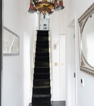 Narrow hallway with white stair case and wooden floor with black stair case runner