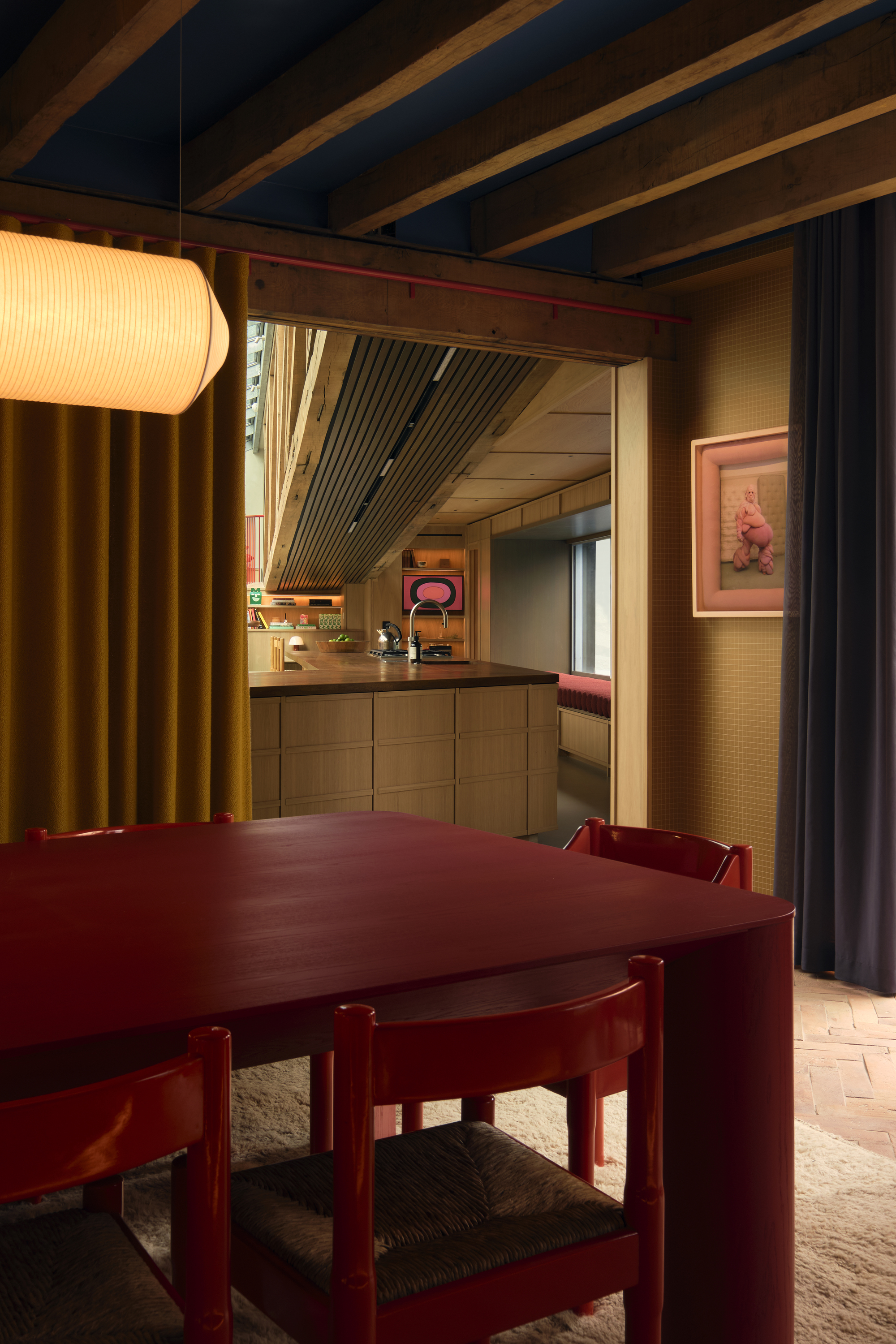 Image of a red dining table and matching red dining chairs in a dark and moody dining room with wooden beams on the ceiling and ochre yellow walls.