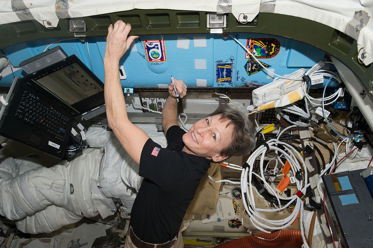 NASA astronaut Peggy Whitson signs a bulkhead on the International Space Station next to the Expedition 50 crew patch, with a Lenovo ThinkPad to the left of frame.