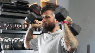 Scott Britton holding dumbbells by his shoulders wearing a pink Whoop tracker on his wrist