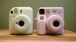 The Fujifilm Instax Mini 12 (left, in green) sits with the Instax Mini SE (right, in purple)