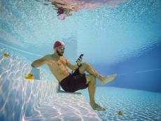 Man underwater in a pool, looking at Starbucks deals on his phone.