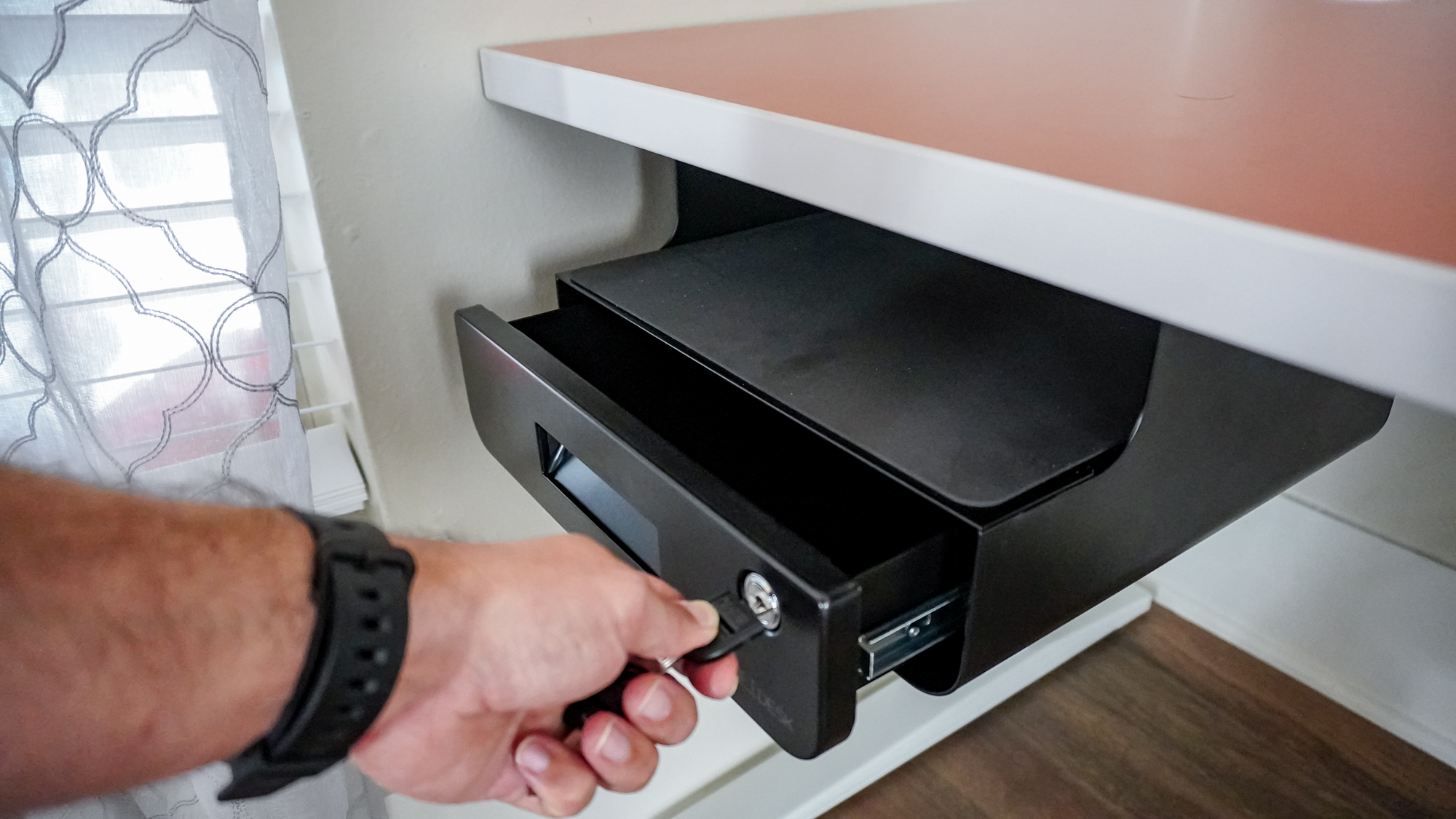 A person showing off the Uplift's lockable under-desk drawer installed on the underside of a desk