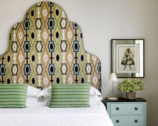 Patterned geometric headboard, white bedding, patterned cushions, bedside table, artwork, mirror, table lamp