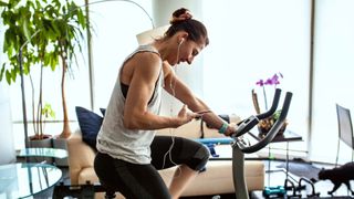 Woman sitting on exercise bike in living room with headphones and workout clothes