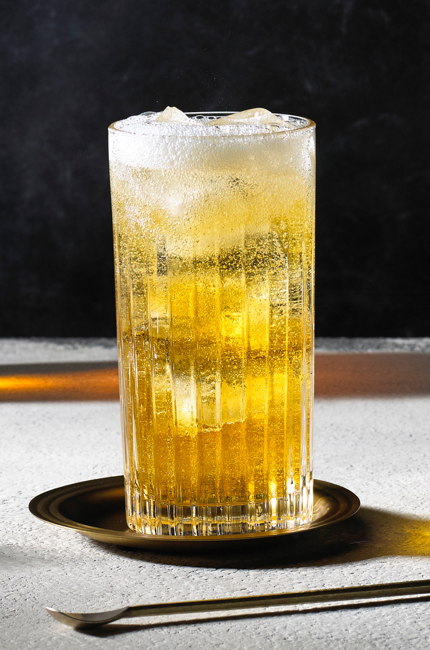 A highball cocktail glass with ice and whisky and soda on a bar top