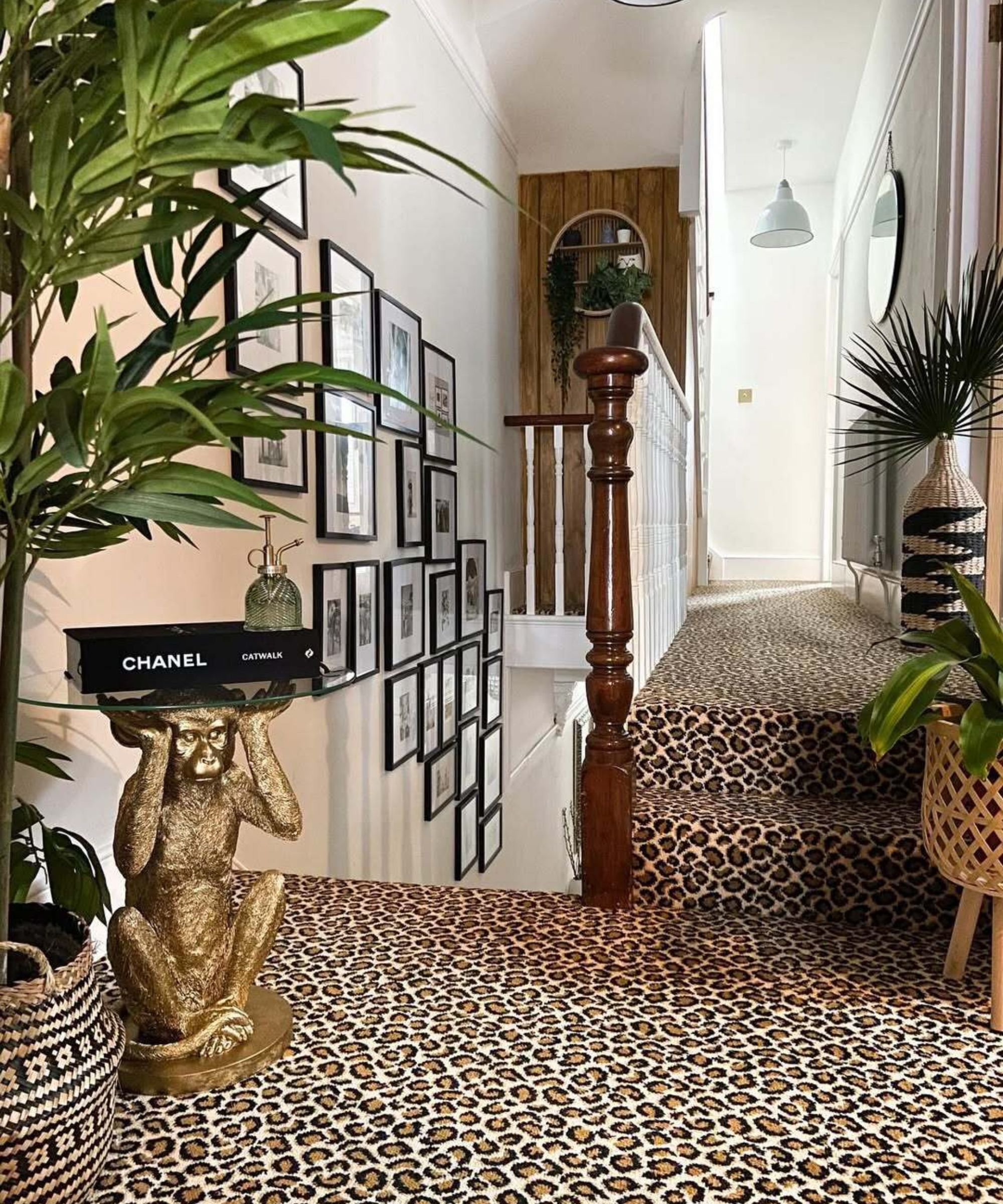 A staircase with leopard print carpet. There are several black and white framed photos on the wall and a gold monkey table