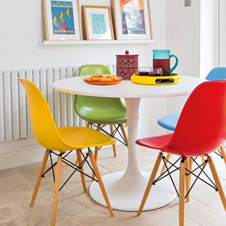 round white table with multi colored plastic chairs and shelf with artwork on it