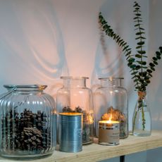Wooden shelf with candles and glass vases holding moss, pine cones and eucalyptus