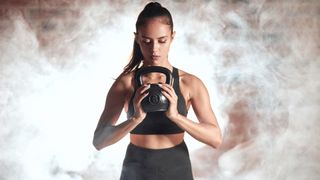Woman holding a kettlebell in both hands with smoke behind her during kettlebell workout
