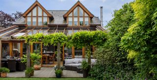 rear exterior of a house with wooden window frames and a generous awning-like structure built over the patio area to demonstrate shadescaping