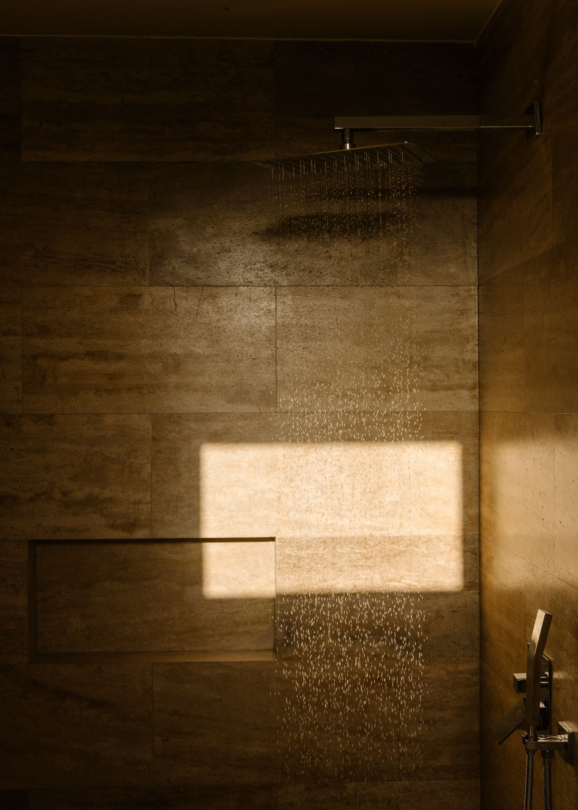 A dimly lit bathroom with a rain shower pouring water